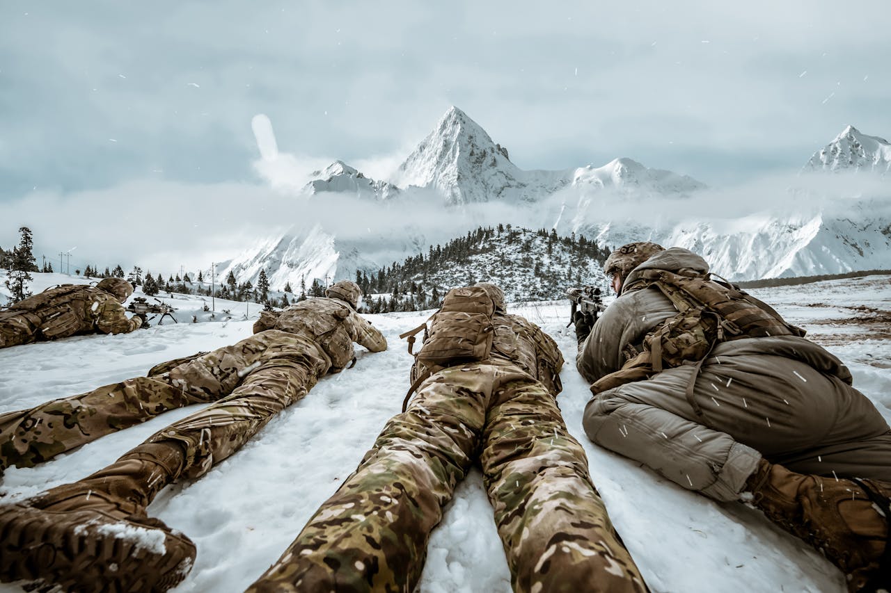Home Soldiers in camouflage lying in snow during winter training in mountain landscape.